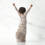 Right back of figure, with arms raised overhead, dress etched with African textile patterns