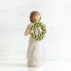 Front view of young girl with bangs and short brown hair holding up a green, leafy wreath