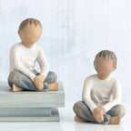Two young boy figurines sitting next to one another in white shirts and blue jeans