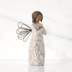 Facing right: angel with wire wings, darker skin, arms crossed over gold heart, dress carved with symbols of remembrance