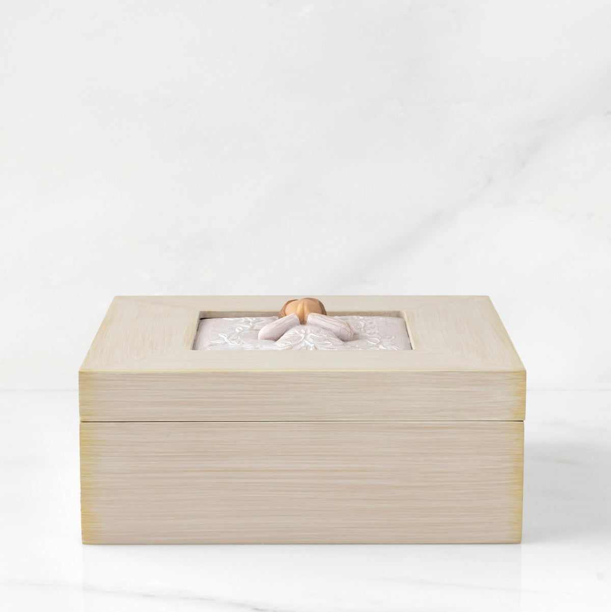 Side View: Cream square wood box with hinged lid, carving on lid of female in cream dress with hands in prayer position, surrounded by leaves and vines