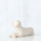 Figure of small white dog laying down with paws crossed in front, facing left