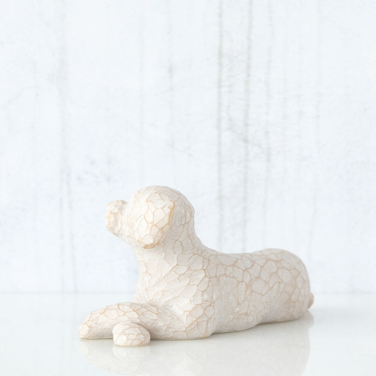 Figure of small white dog laying down with paws crossed in front, facing left