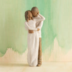 Front view of couple, standing with arms around each other. Woman and man have darker skin tones and hair color. Green painted background.