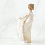 Brunette girl figurine holding up white and gold polka dot dress facing the side
