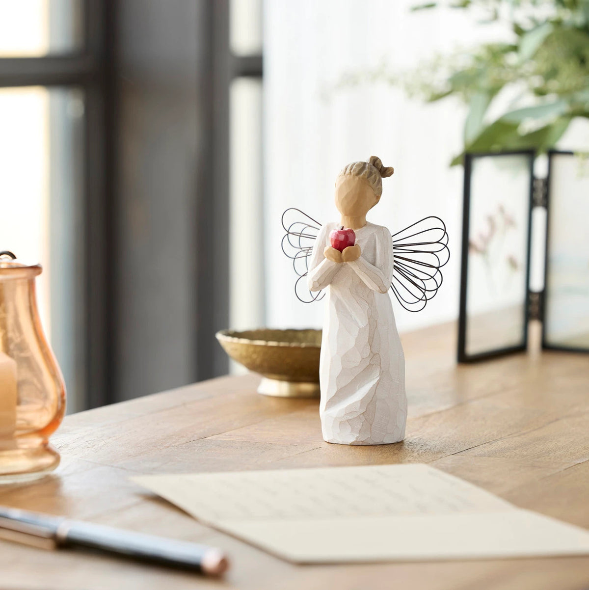 Willow Tree You're The Best!, 5.5”h hand-painted standing resin angel figure in cream dress with wire wings, holding red apple in outstretched hands, on desk with letter