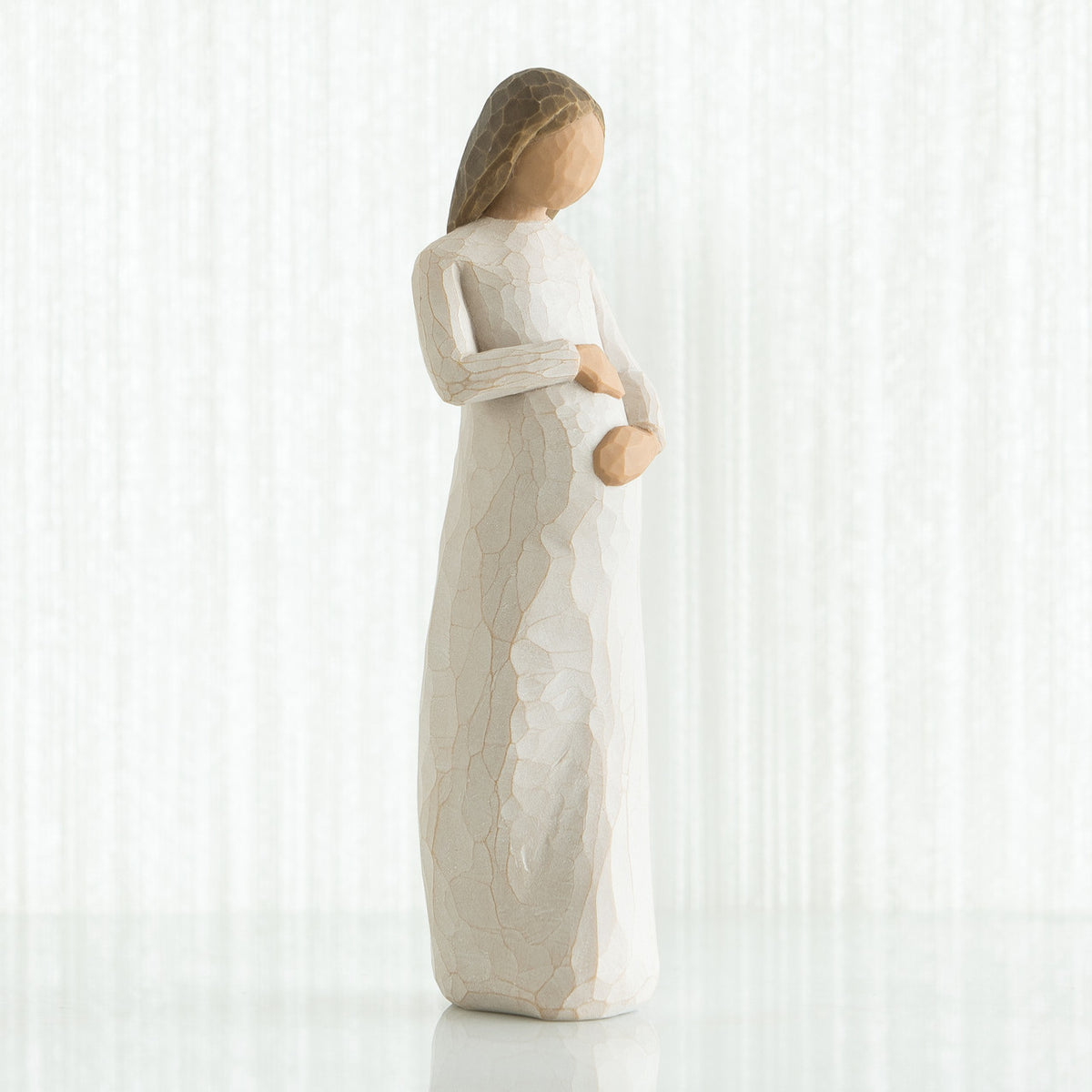 Faceless pregnant woman figurine wearing white dress with hands clutching her stomach