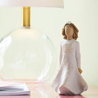 Willow Tree Irish Charm, 5.5" hand-painted dancing resin figure in cream dress with full skirt carved with stylized Celtic knot, arms down to sides, wire crown of hearts, on table with glass lamp