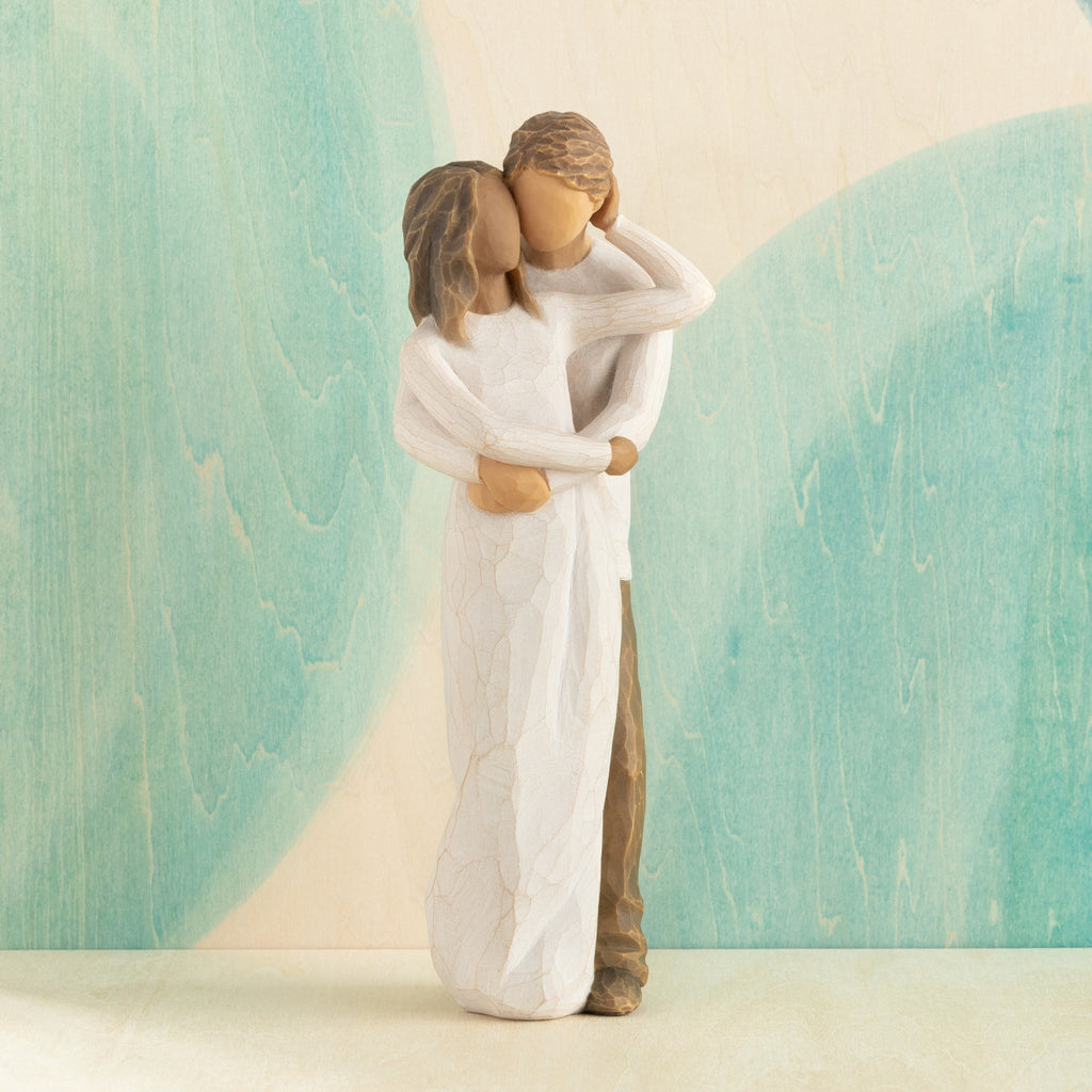 Front view of couple, standing with arms around each other. Woman has darker skin and hair; man has lighter skin and hair. Blue painted background.