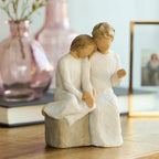 Willow Tree With my Grandmother, 5.5" hand-painted resin figure of older woman seated on gray bench, holding hands with young girl, both in cream dresses, on table with vase