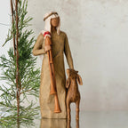 Wiseman figurine in tan dress next to golden lamb figurine with green tree in the background