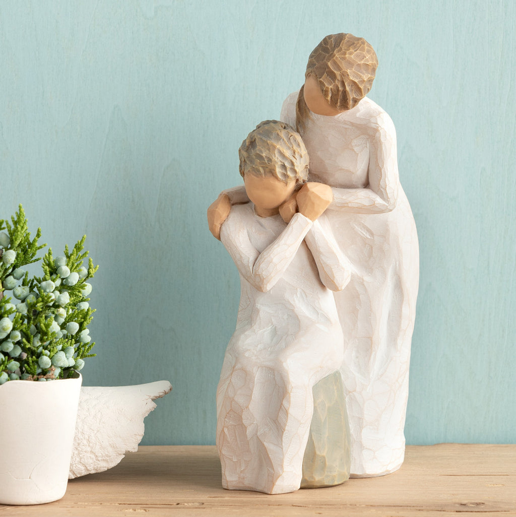 Willow Tree Loving My Mother, 6.5”h hand-painted resin figure of seated older woman with younger woman standing at her shoulder, both in cream dresses, hands clasped, in front of muted teal painting