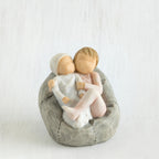 Two small baby figurines hugging another laying on grey beanbag