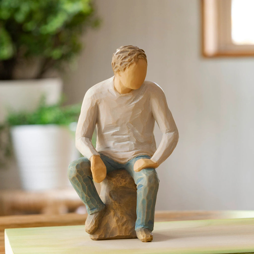 Willow Tree My Guy, 6”h hand-painted resin adult figure in light gray shirt and jeans, seated on gray rock, on wooden table