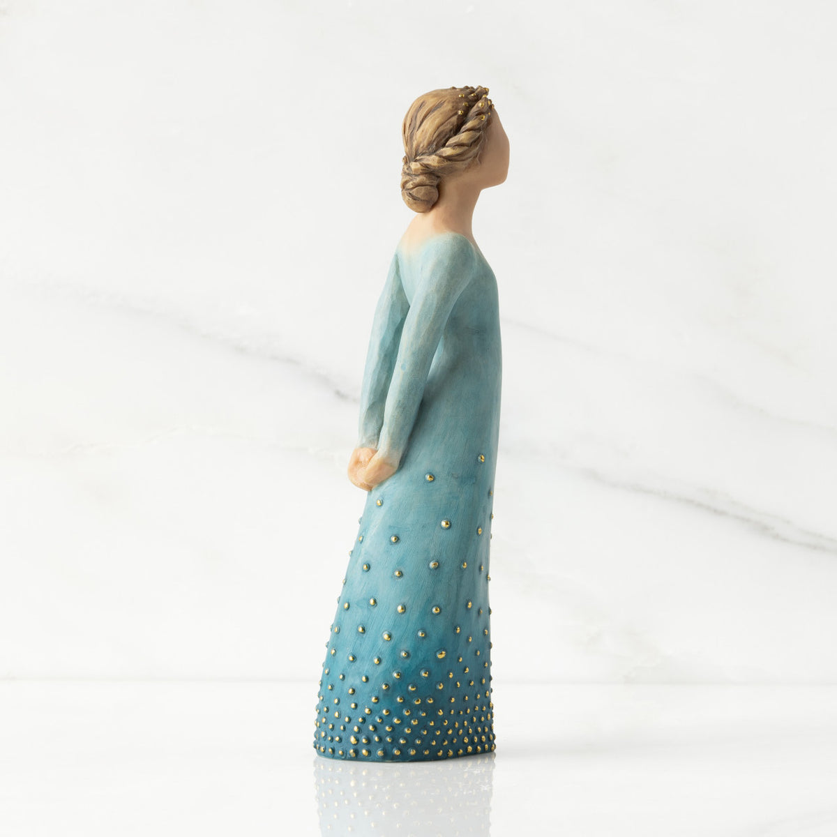 Facing right profile: Lighter-skin figure, arms clasped behind back, hair and deep blue ombré garment dotted with gold leaf