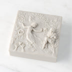 Closed white resin square box; lid carved with figural and organic imagery