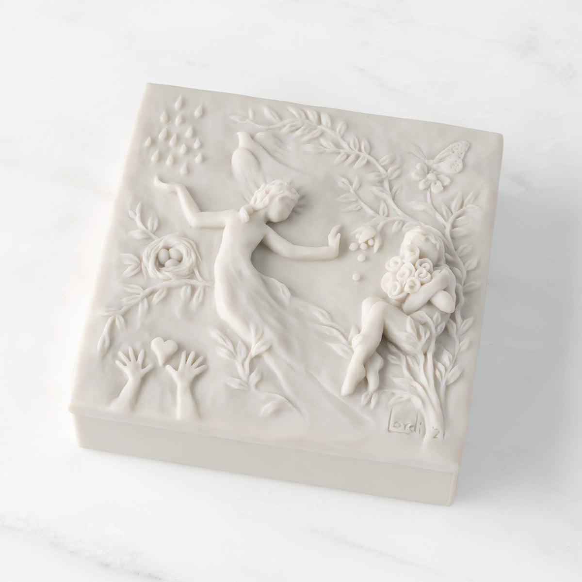 Closed white resin square box; lid carved with figural and organic imagery