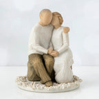 Two faceless figurines - one man and one woman sitting hugging one another on a rock