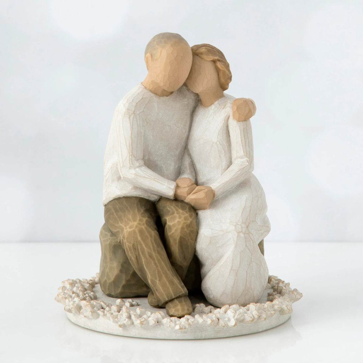 Two faceless figurines - one man and one woman sitting hugging one another on a rock