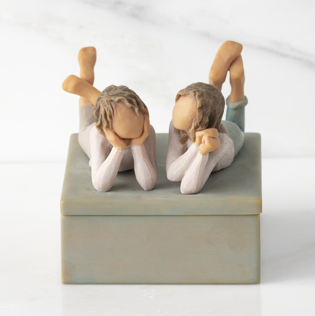 Front view of closed rectangular blue-gray resin box, sculpture of two girls affixed to lid