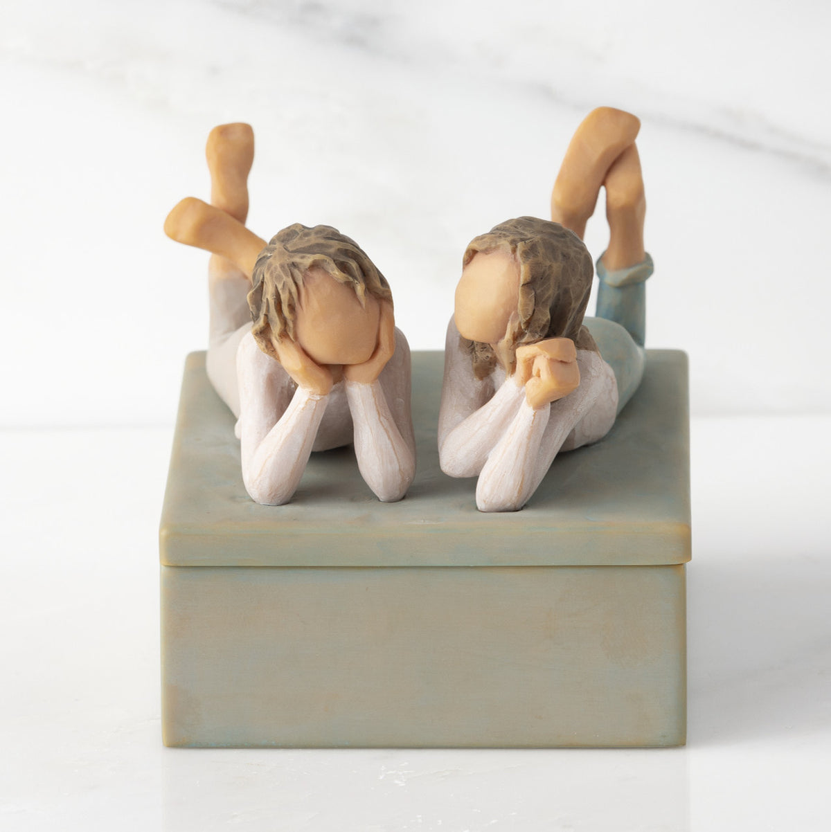 Front view of closed rectangular blue-gray resin box, sculpture of two girls affixed to lid