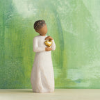 Willow Tree Keepsake, 5.5”h hand-painted standing resin figure with darker skin and hair, in cream dress, framing gold heart with both hands on her chest, in front of green painting