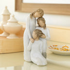 Willow Tree Our healing touch, 6.5”h hand-painted resin figure of three women; one standing with arm around kneeling girl, holding hand of seated girl, kneeling girl arranging hair of seated girl, all in cream dresses, on bedside table