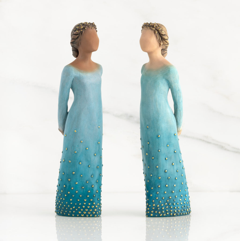 Front view of both lighter and darker-skin figures, arms clasped behind backs, hair and deep blue ombré garments dotted with gold leaf.