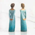 Back view of both lighter and darker-skin figures, arms clasped behind backs, hair and deep blue ombré garments dotted with gold leaf.